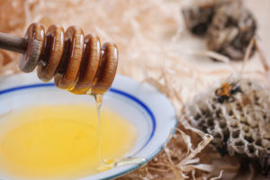 Plate of honey with wild honeycombs and bee over wooden table