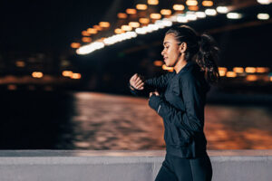 Young middle east woman jogging at night looking in fitness tracker on her wrist